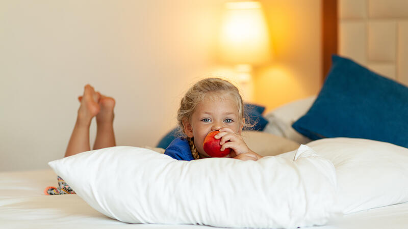 Little girl eating ripe juicy fruit on bed at home.
